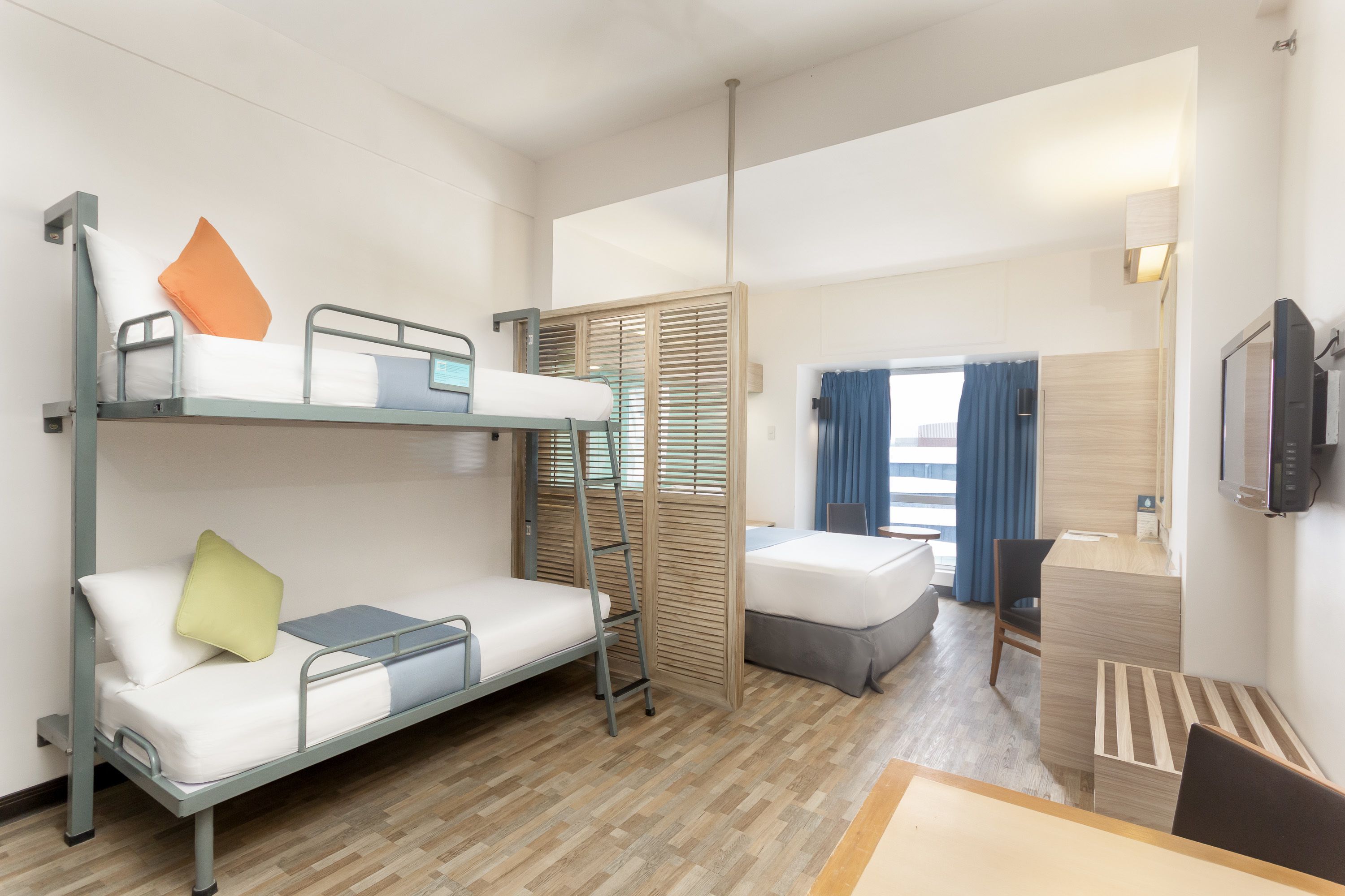Habitación de hotel con literas, un escritorio, una silla, un televisor y una ventana con cortinas.