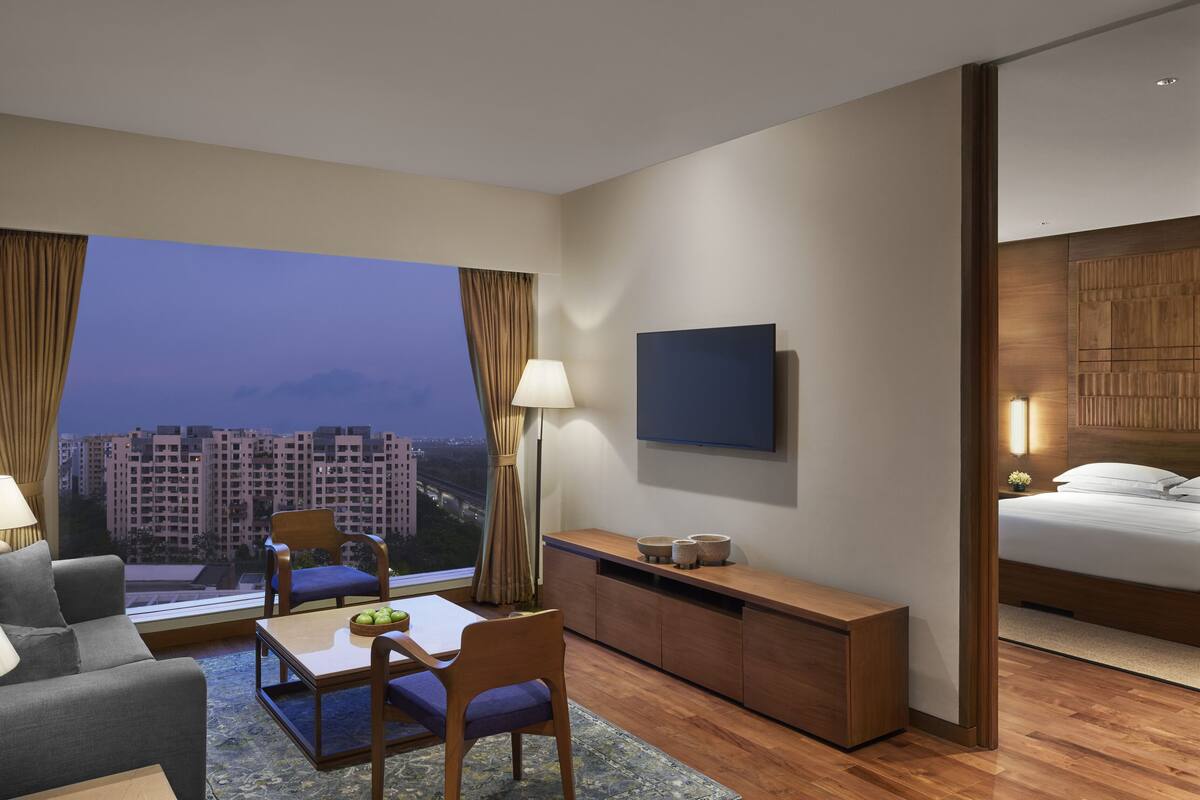 A hotel room with a large window, a bed, a desk, a chair, a sofa, and a TV.
