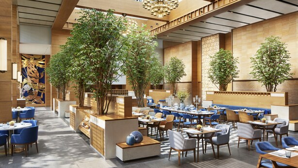 A spacious indoor dining area with multiple tables and chairs, large windows, and indoor plants. - Taj City Centre New Town Kolkata (Barasat)