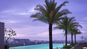 An infinity pool with a city view, surrounded by palm trees and lounge chairs. - Taj City Centre New Town Kolkata (Barasat)