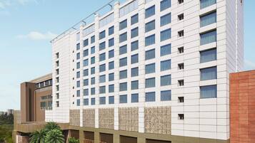 Un hôtel moderne, reconnaissable à son grand panneau « TAJ », avec une façade ornée d’un motif et une série de fenêtres disposées en réseau.
