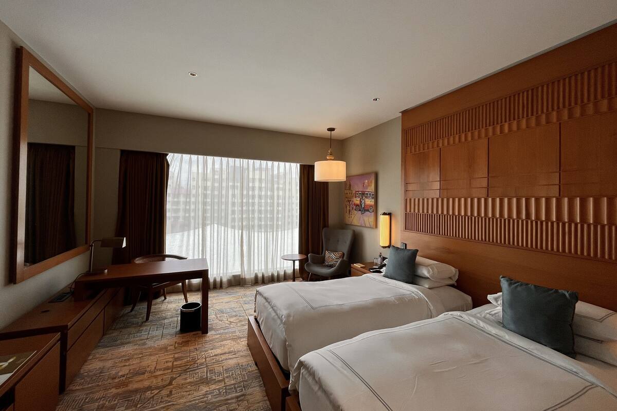 A hotel room with two beds, a desk, a chair, a lamp, and a large mirror.
