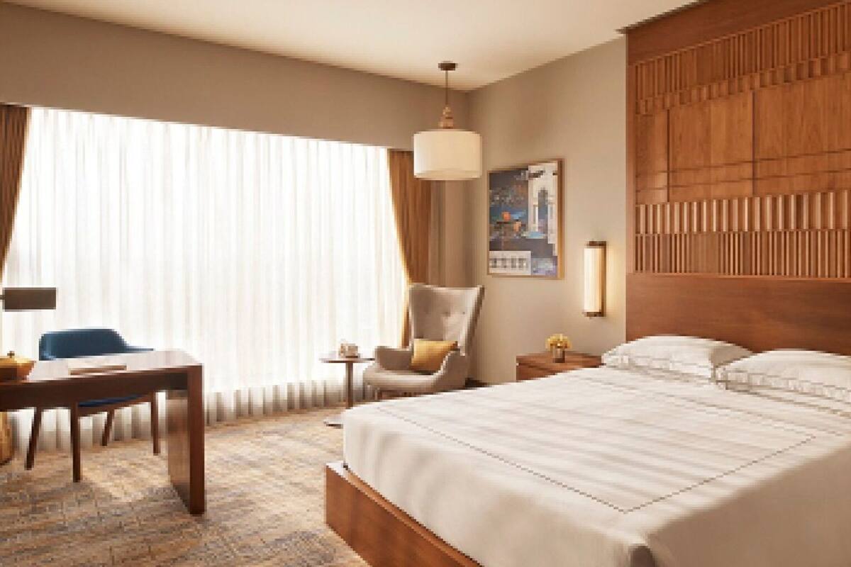 A hotel room with a large bed, a desk, a chair, and a window with curtains.