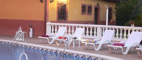 A swimming pool with lounge chairs and a building with a tiled roof.