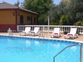 A swimming pool with lounge chairs and a small building with a tiled roof.