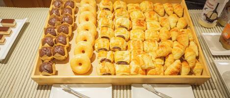 Tarjottimella on erilaisia leivonnaisia, kuten muffinseja, donitseja ja croissantteja.