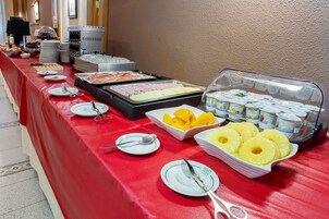 Une table de buffet proposant une variété d’aliments, notamment des fruits, des yaourts et un espace dédié aux plats chauds.