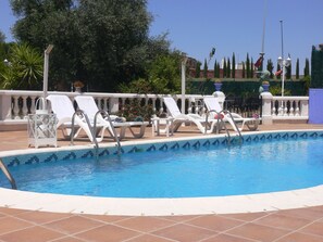 A swimming pool with white lounge chairs and a tiled deck.