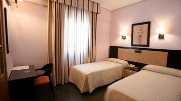 A hotel room with two beds, a desk, a chair, and a window with curtains.