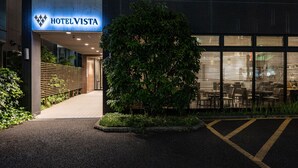 A hotel entrance with a sign reading "HOTEL VISTA," a paved walkway, a small tree, and a parking area. - Hotel Vista Ebina (Ebina)