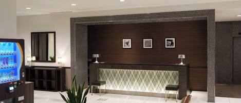 A modern lobby with a reception desk, seating area, and a vending machine.