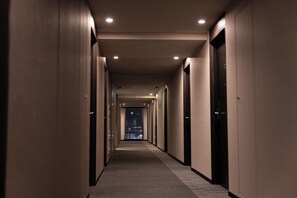 Un largo y estrecho pasillo de hotel con puertas a ambos lados, que conduce a habitaciones individuales.