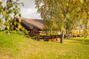 En rustik træbygning med et skråt tag, omgivet af en græsplæne med picnicborde.