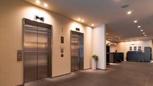 A modern elevator area with two elevators, a reception desk, and a potted plant.