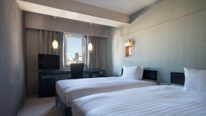 A hotel room with two beds, a desk with a TV, and a window with curtains.