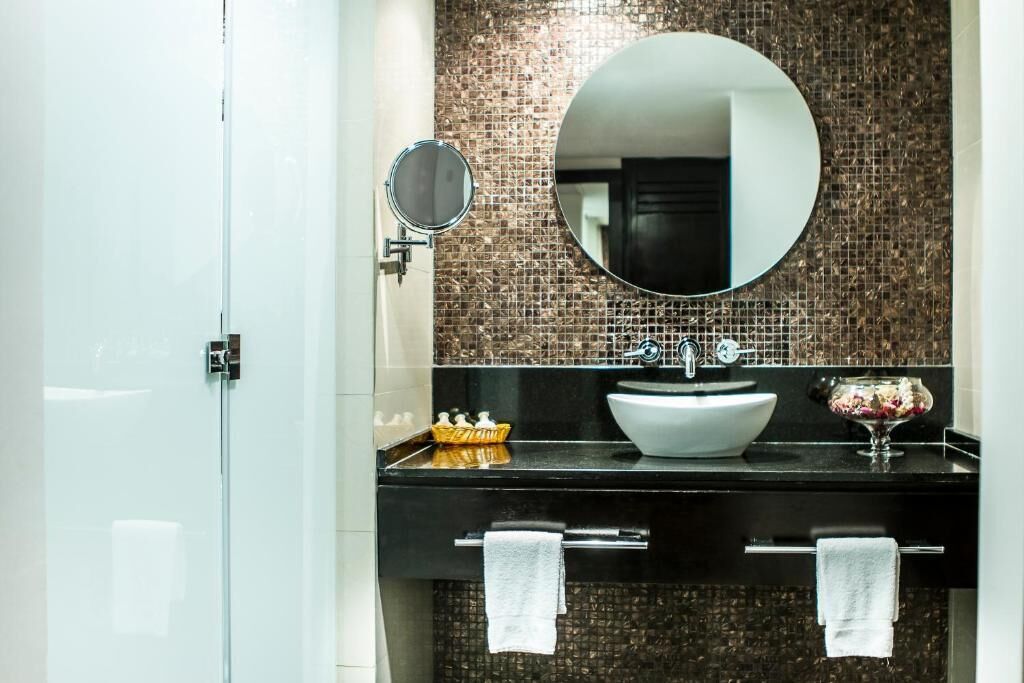 Ein modernes Badezimmer mit schwarzem Waschtisch, weißem Waschbecken, einem runden Spiegel und einer Rückwand aus Mosaikfliesen.