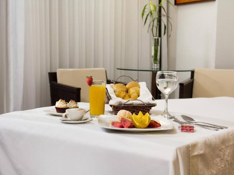 A breakfast table with a basket of pastries, a glass of orange juice, a plate of fruit, and a cup of coffee.
