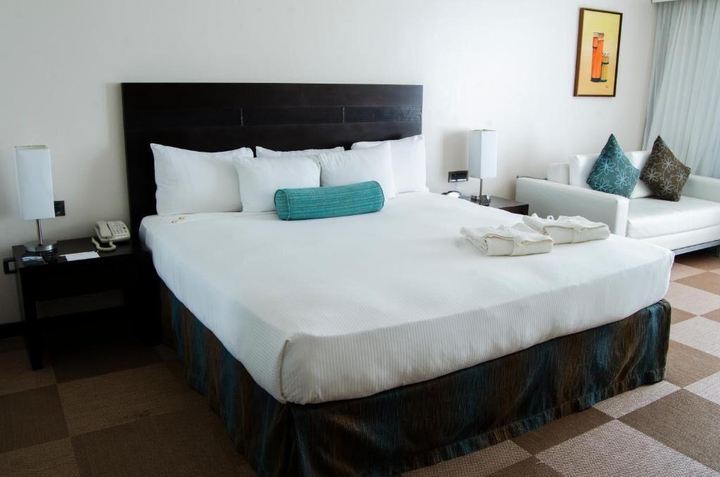 Een hotelkamer met een groot bed, een nachtkastje met een telefoon, een bank en een aan de muur hangend schilderij.