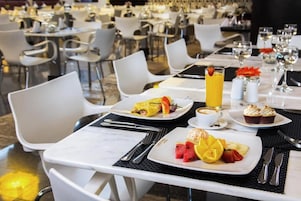 Mesa de jantar com itens de café da manhã, incluindo omelete, frutas e uma bebida com café.