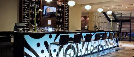 A bar area with a long counter, multiple bar stools, and a television screen mounted above the bar.