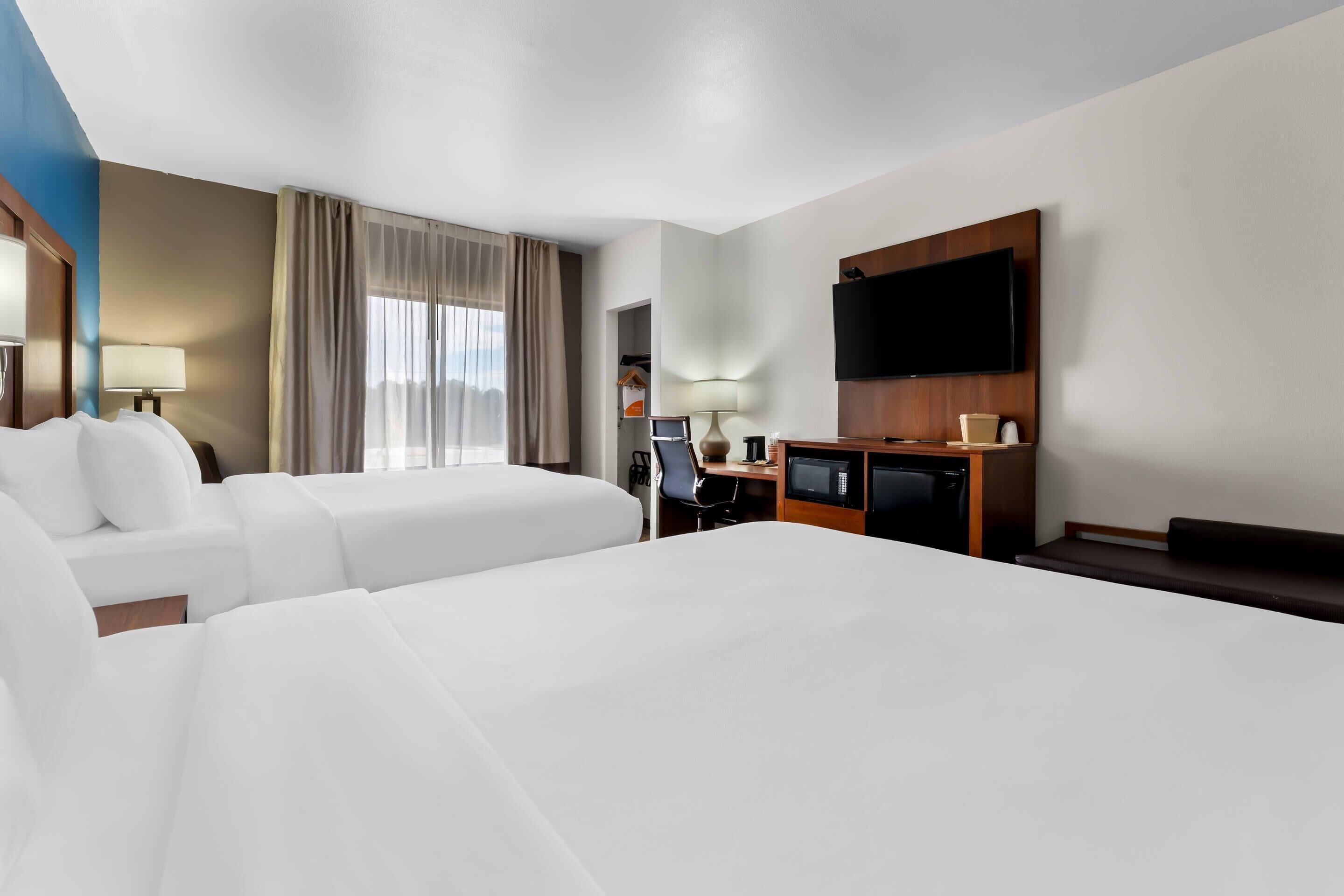A hotel room with two large beds, a desk with a flat-screen TV, a microwave, and a seating area.