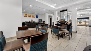 A hotel dining area with multiple tables and chairs, a kitchen in the background, and a large mirror on the wall. - Comfort Inn & Suites Augusta West Near Fort Gordon (Augusta)