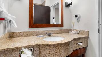 Baño con lavamanos de encimera de granito, espejo, toallero, secador de pelo y dispensador de toallas.