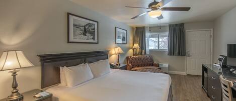 Hotelkamer met een groot bed, twee bedlampen, een plafondventilator, een bureau met stoel en een televisie.