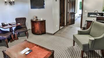 Quarto de hotel com área de estar, incluindo uma mesa de centro, poltronas, uma TV e um pequeno armário.