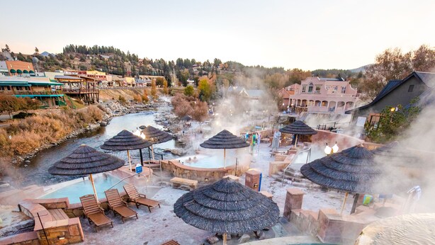 A hot spring resort with a central pool, lounge chairs, and thatched umbrellas. - The Springs Resort & Spa (Pagosa Springs)