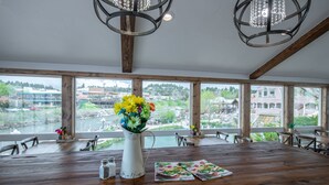 A wooden dining table with a vase of flowers, salt and pepper shakers, and a menu. Large windows offer a view of a river and buildings. - The Springs Resort & Spa (Pagosa Springs)