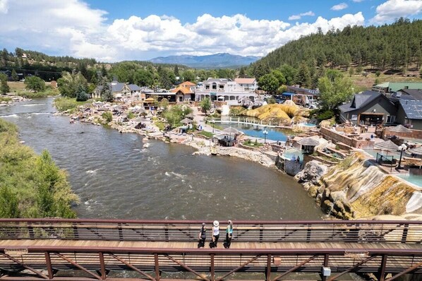 Un pueblo a orillas del río con un puente, edificios y el río.