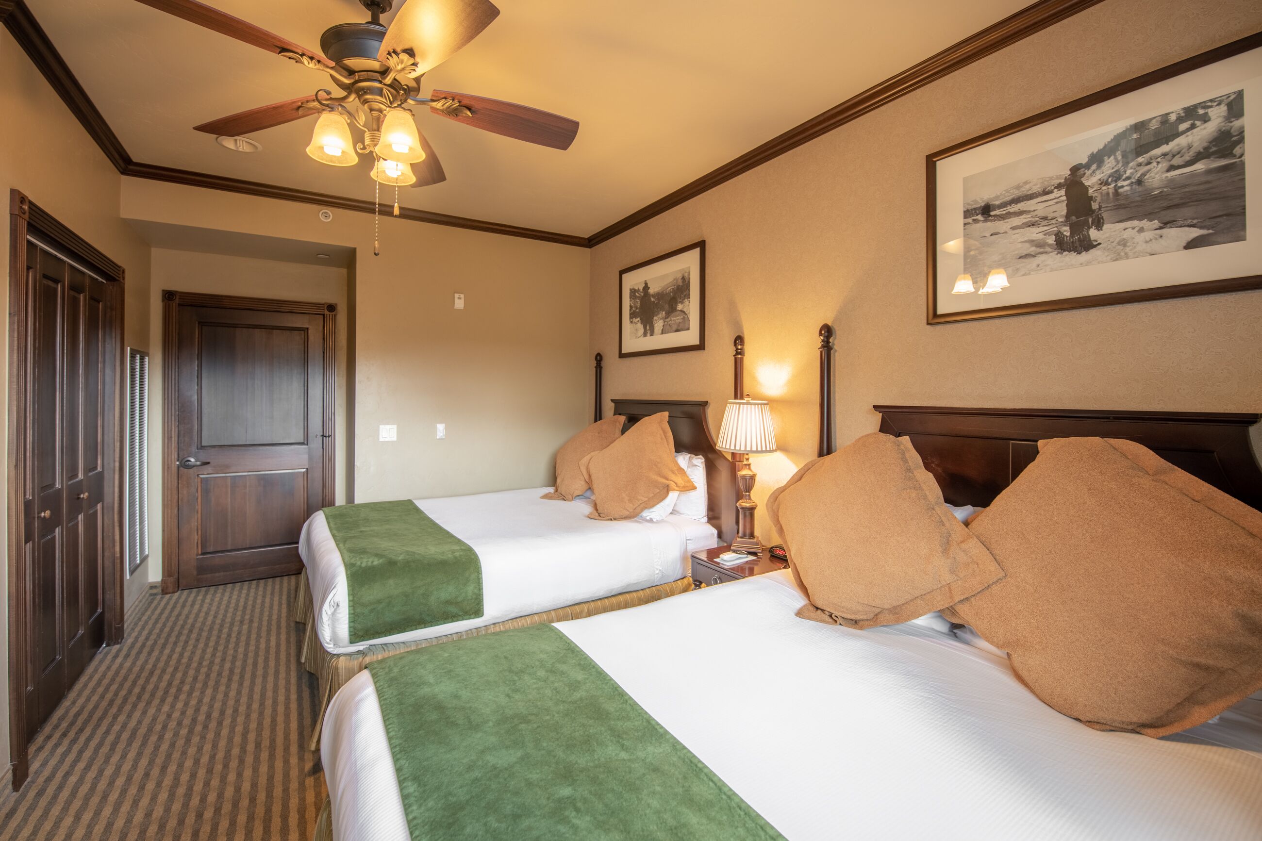 A hotel room with two beds, a ceiling fan, a framed picture on the wall, and a door.