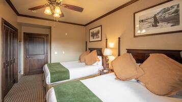 A hotel room with two beds, a ceiling fan, a framed picture on the wall, and a door.