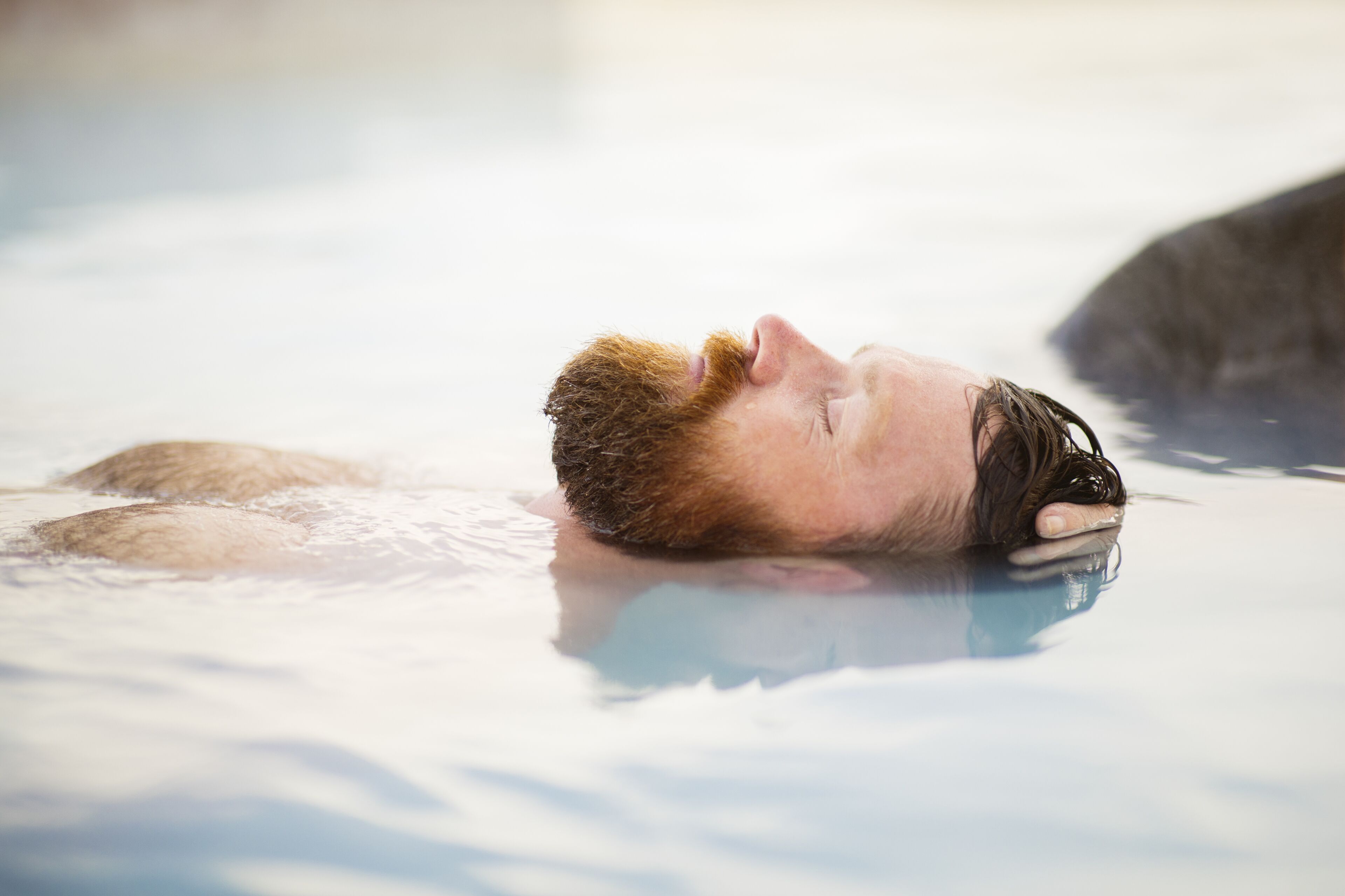 Una persona relajándose en un manantial termal, con vapor visible elevándose del agua.