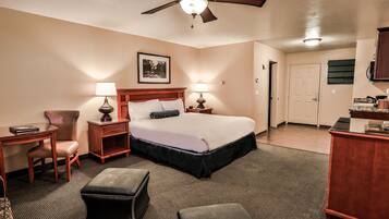 A hotel room with a bed, two bedside tables with lamps, a desk, a chair, and a ceiling fan.