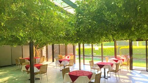 Un espace de restauration intérieur avec des tables et des chaises, de grandes fenêtres et une vue sur un jardin bien entretenu.