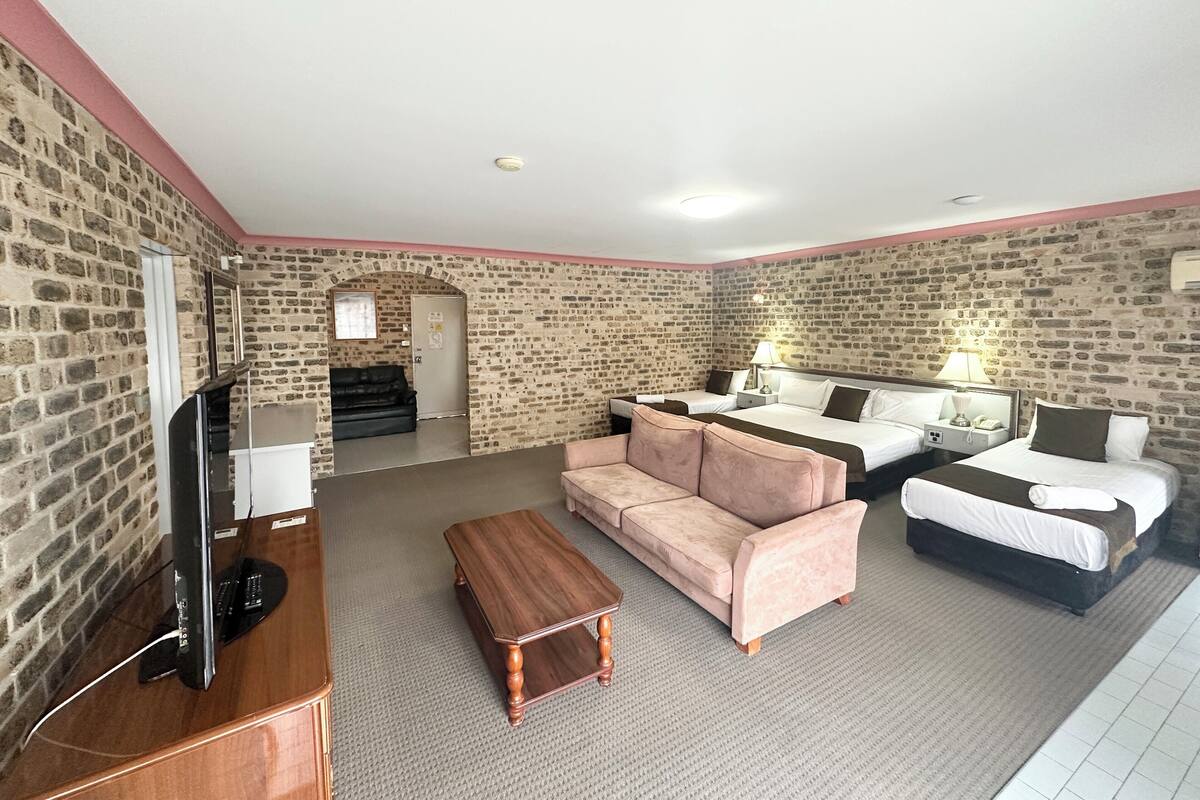 A hotel room with a brick wall, a flat-screen TV, a sofa, a coffee table, and a bed with two pillows.