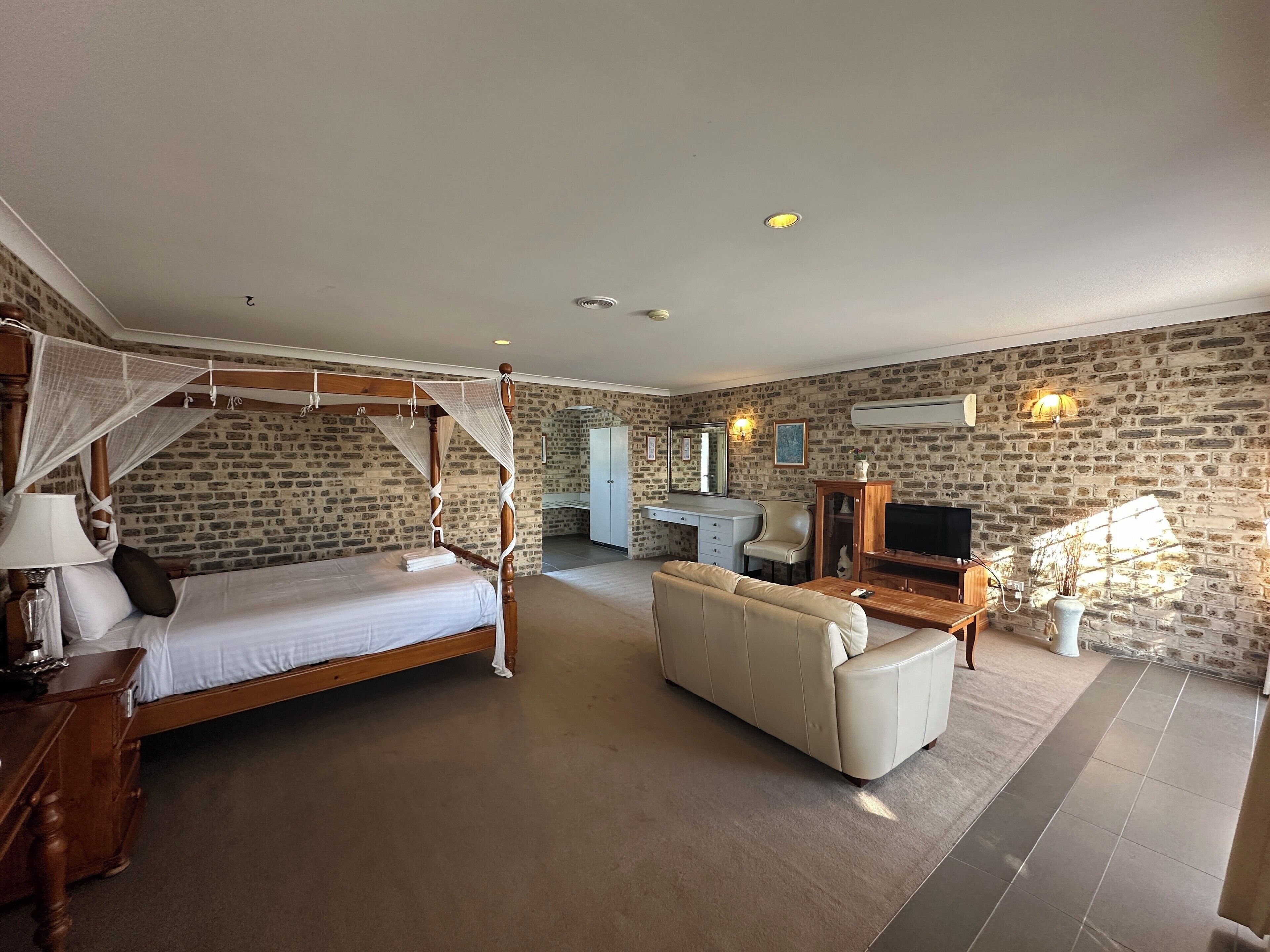 A bedroom with a four-poster bed, a sofa, a desk, and a television.