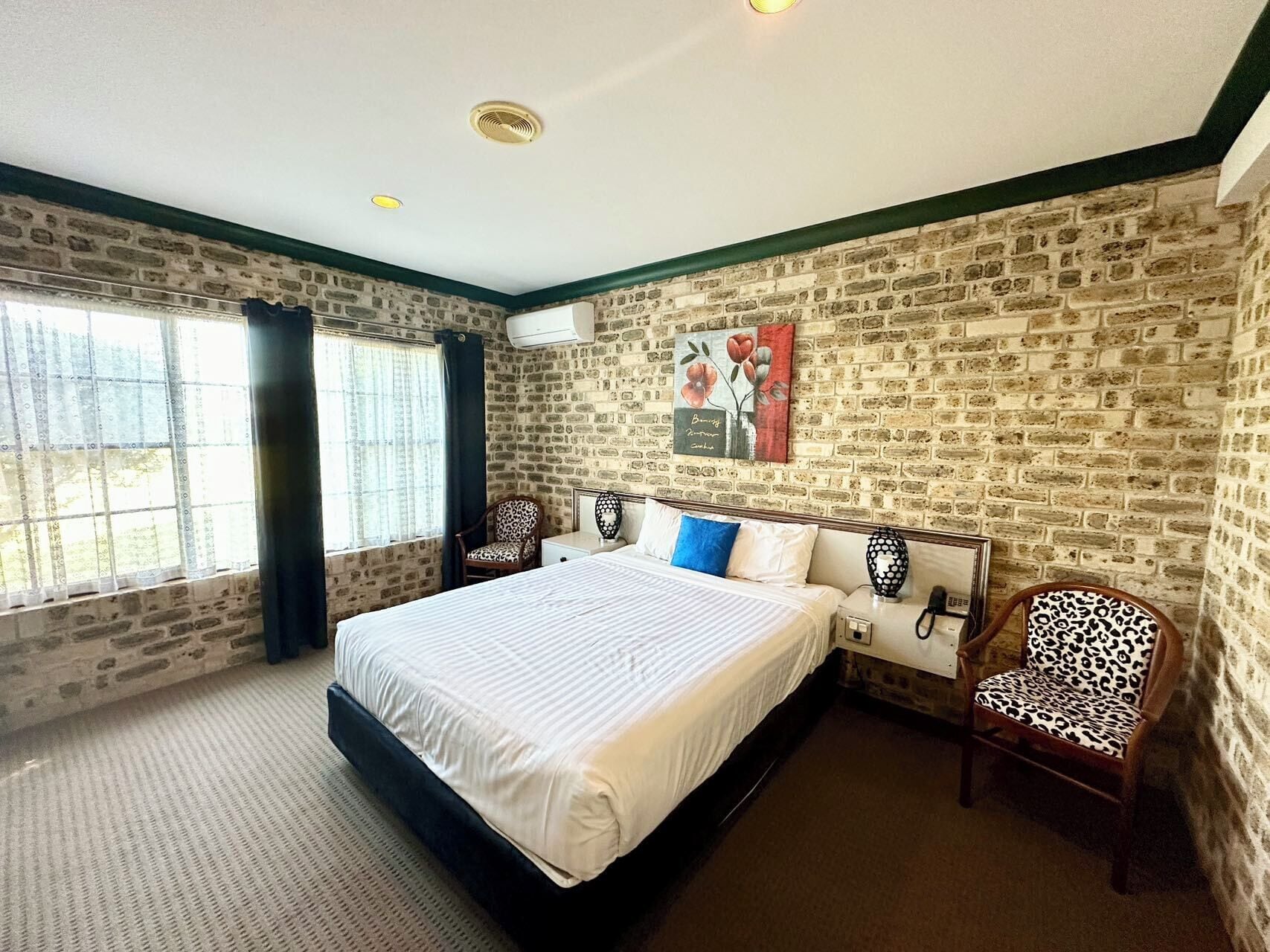 A bedroom with a large bed, a chair, a nightstand, and a window with curtains.