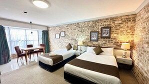 Une chambre d’hôtel avec deux lits, un coin repas et un mur en briques.
