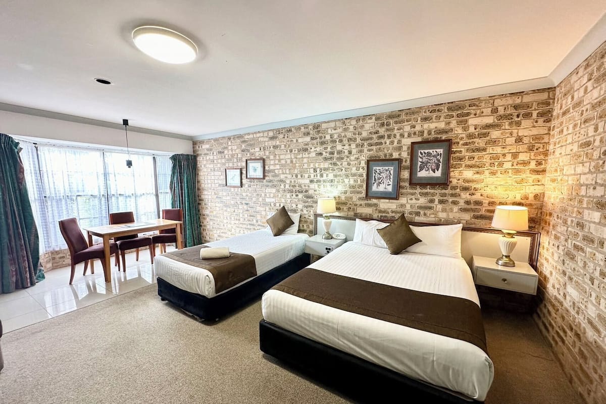 A hotel room with two beds, a dining area, and a brick wall.