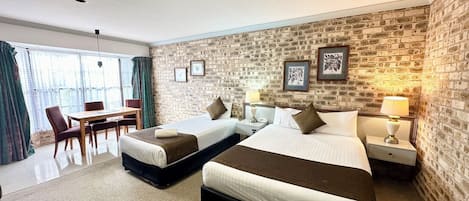 Habitación de hotel con dos camas, un comedor y una pared de ladrillo.