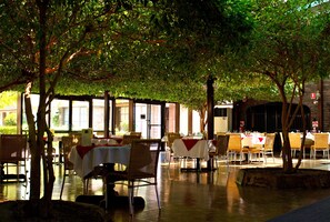 An outdoor dining area with tables and chairs, surrounded by trees.
