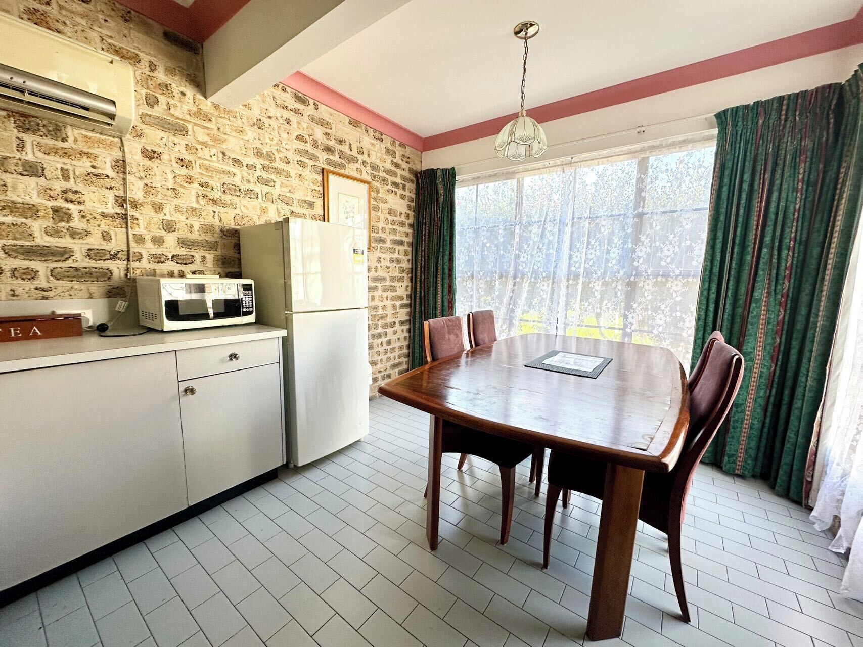 Una cocina con pared de ladrillo, un refrigerador blanco, un microondas y una mesa de comedor con sillas.