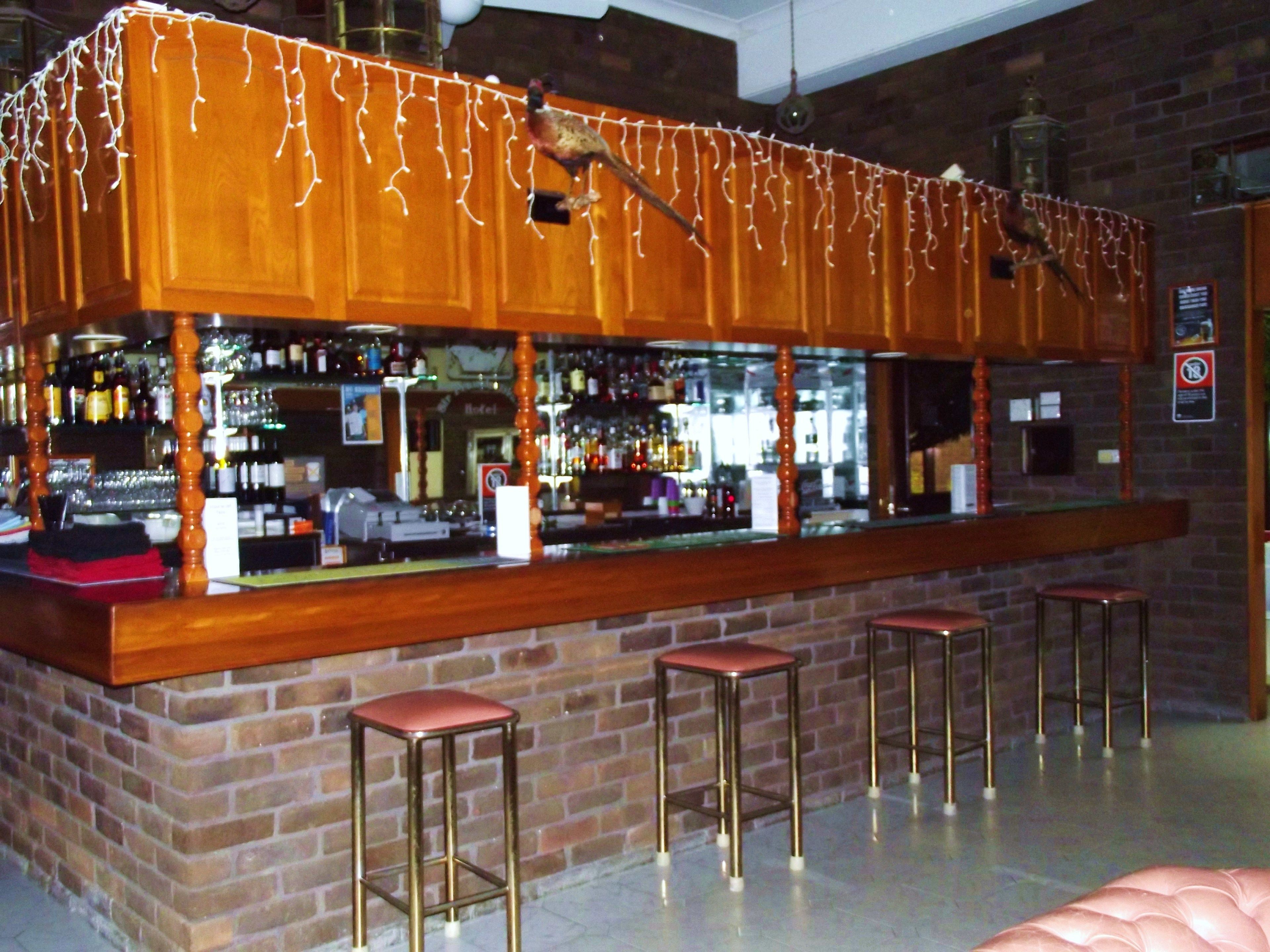 A bar area with wooden counters, multiple stools, and a brick wall backdrop.