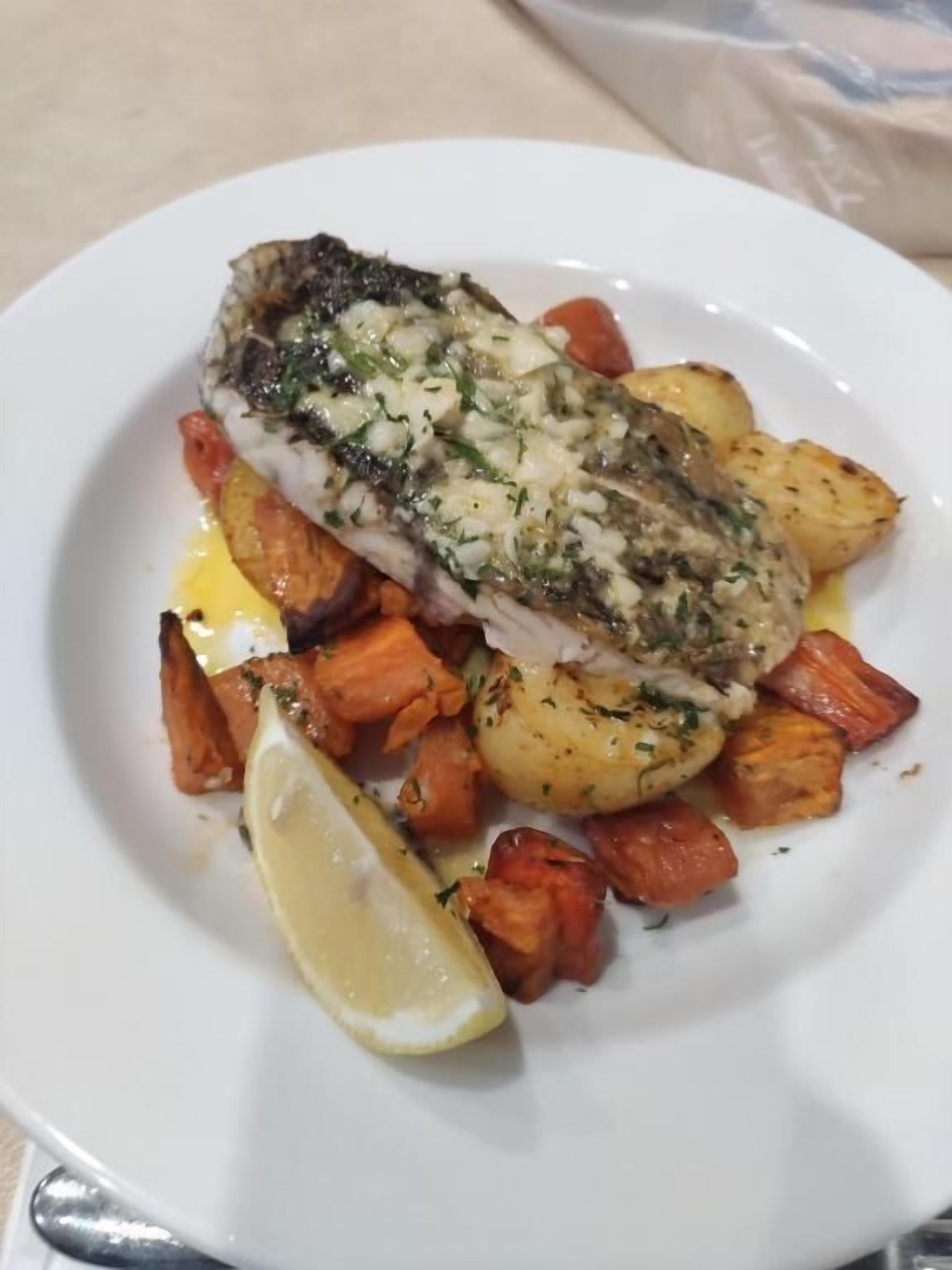 Un plato con un filete de pescado, patatas asadas y un gajo de limón.