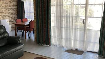 Una sala de estar con un sofá de cuero, una mesa de centro de madera, un comedor con mesa y sillas, y un ventanal con cortinas.