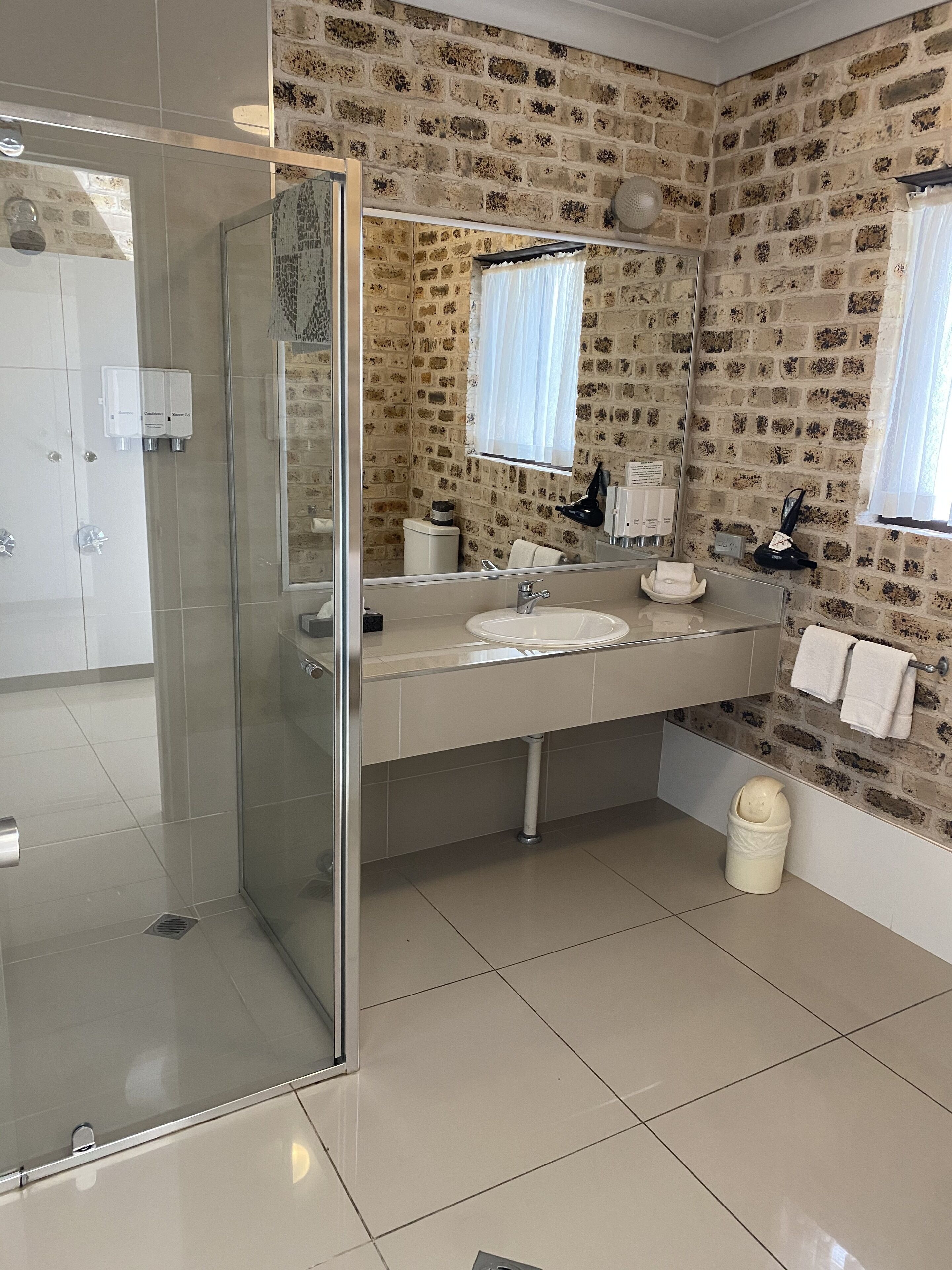 A bathroom with a glass shower enclosure, a sink with a mirror, and a tiled floor.