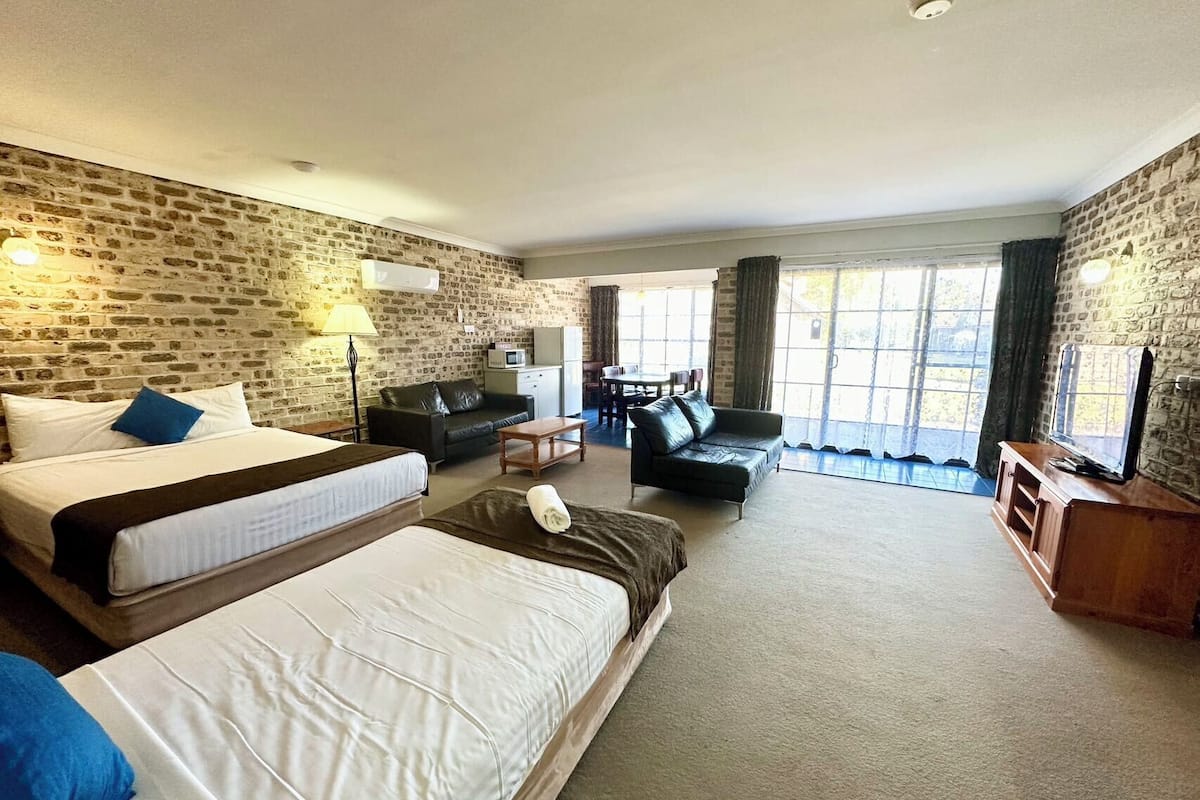 A hotel room with two beds, a sofa, a TV, and a dining area with a table and chairs.